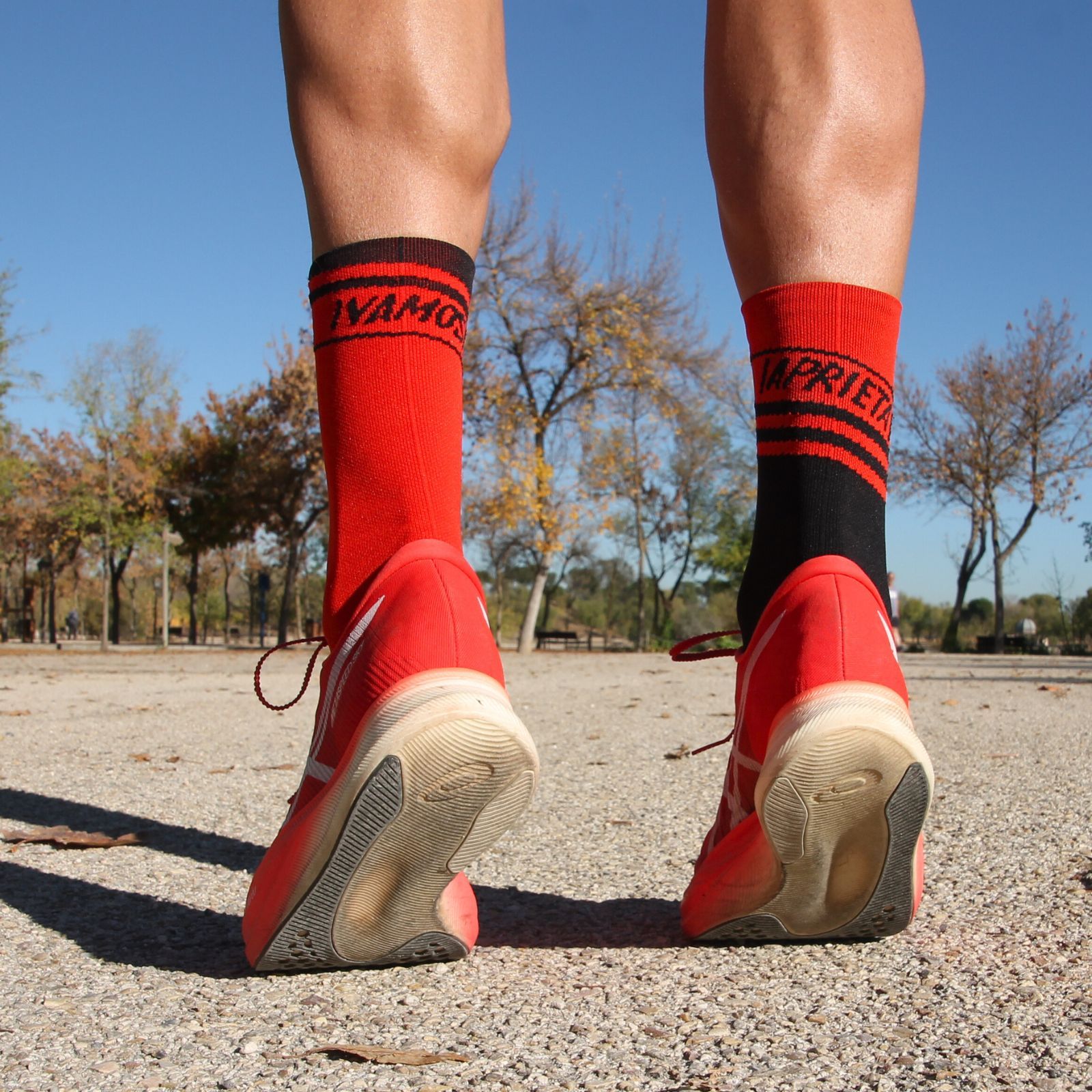 Imagen de pies de un corredor de puntillas vistiendo calcetines de color rojo y negro con la frase inspiradora Vamos Aprieta para la categoría de calcetines deportivos